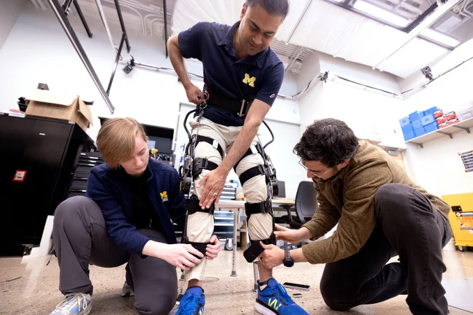 Two researchers adjust a motorized knee exoskeleton worn by another researcher.