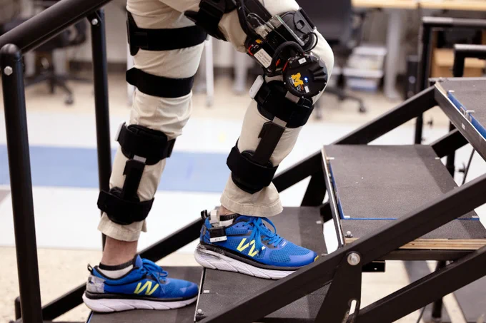 A person wearing a motorized knee exoskeleton walks on a staircase in a laboratory.
