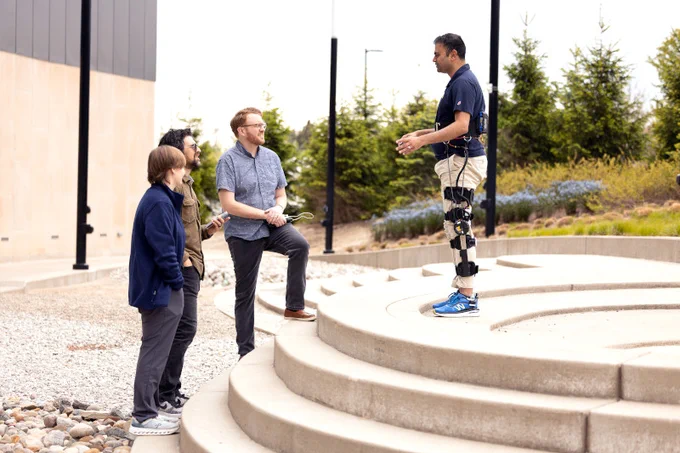 Researchers observe a person wearing a motorized knee exoskeleton outdoors near the Ford Robotics Building.