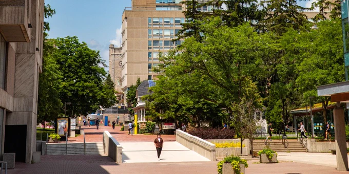 A distant figure walks through the quad at the University of Guelph on a sunny day. 