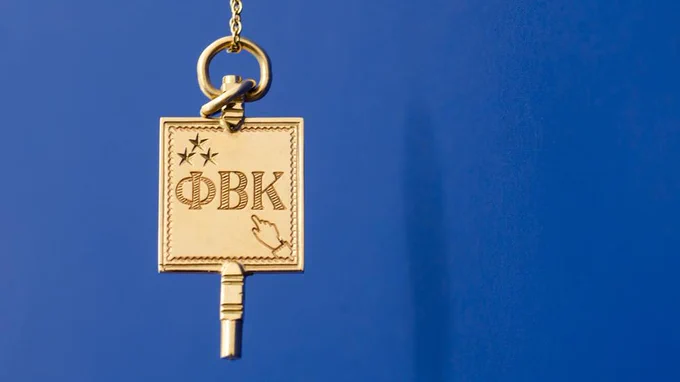 A gold key with a rectangular bow hangs against a blue background. The key features engraved stars, the Greek letters ΦΒΚ, and an image of a pointing hand.