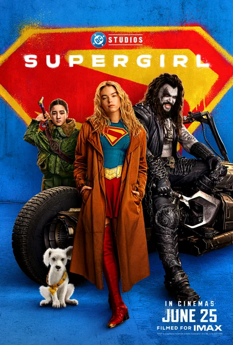 A poster for Supergirl, featuring three characters posing in front of a red and yellow stylized backdrop. One character stands in the center wearing a Supergirl suit and a long brown coat. To the left is another character in a green outfit. To the right is a character sitting on a vehicle weather a black leather outfit with painted white face and black markings around their eyes. Additionally, there is a white dog in the foreground. Text at the bottom reads, "In cinemas June 25, filmed for IMAX."
