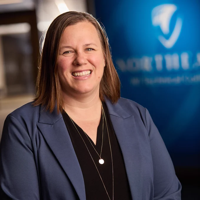 A professional headshot of a woman with a blurred logo in the background.