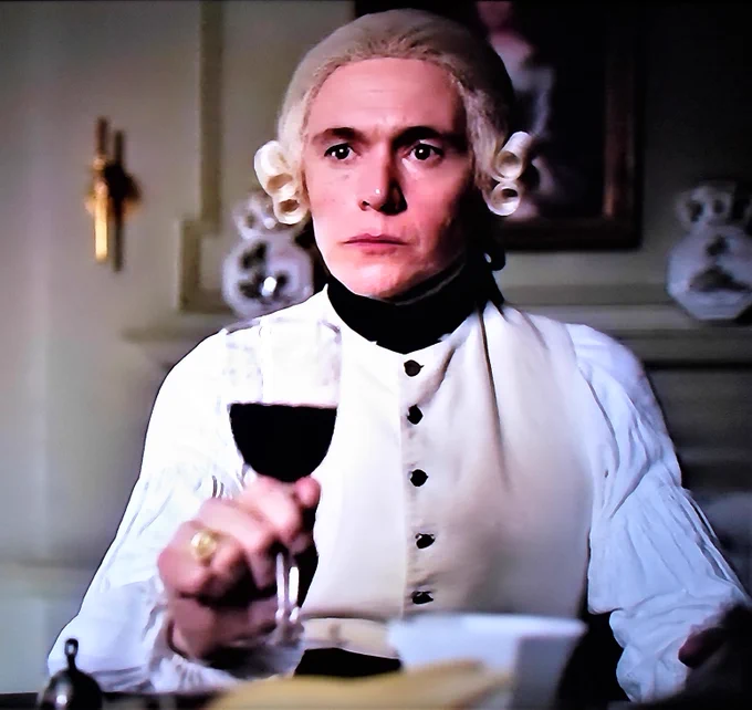 Burn Gorman as Major Edmund Hewlett holding a glass of red wine, coatless at the Whitehall dining table. He looks unhappy. TURN: Washington's Spies E107