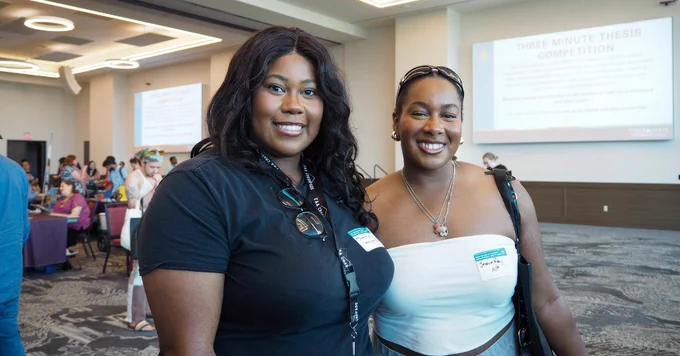 Two women posing together at a conference room during a graduate student orientation event.
