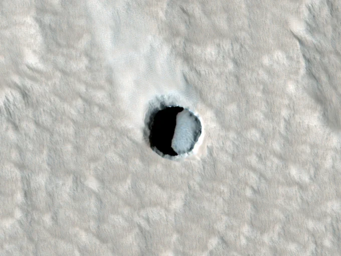 Enhanced color cutout shows a small pit on the surface of Mars. The bottom of the pit is visible, but it could also be a small cave.