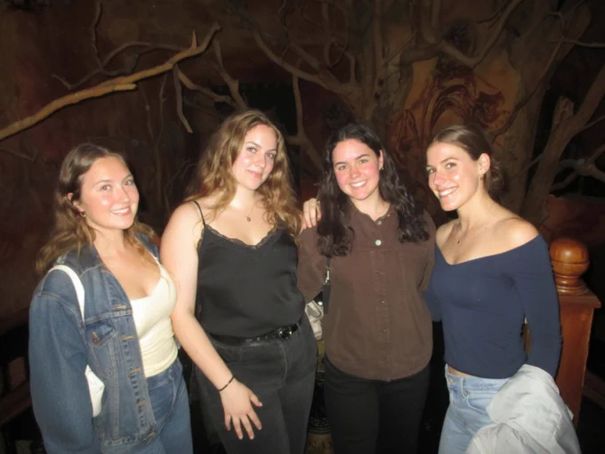 Four students smiling at night with tree branches in the background.