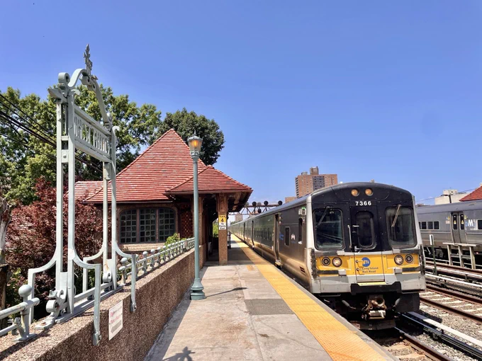 An LIRR train pulling into Forest Hills station on a sunny day.