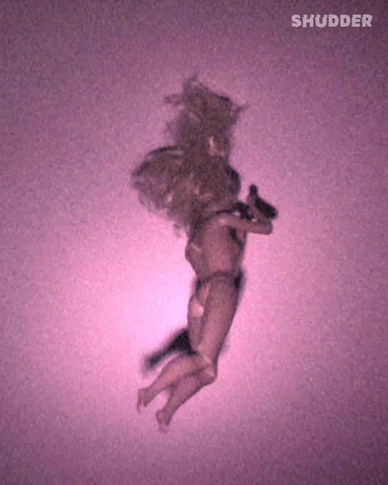 A doll floats against a purple, grainy background, casting a mysterious and eerie mood. The scene is enhanced by a visual effect simulating nighttime or low-light conditions.