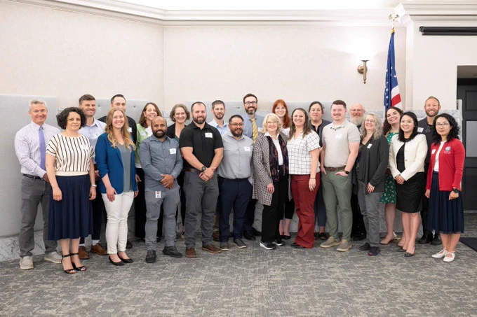 Group of diverse professionals standing together in a conference room with an American flag in the background.