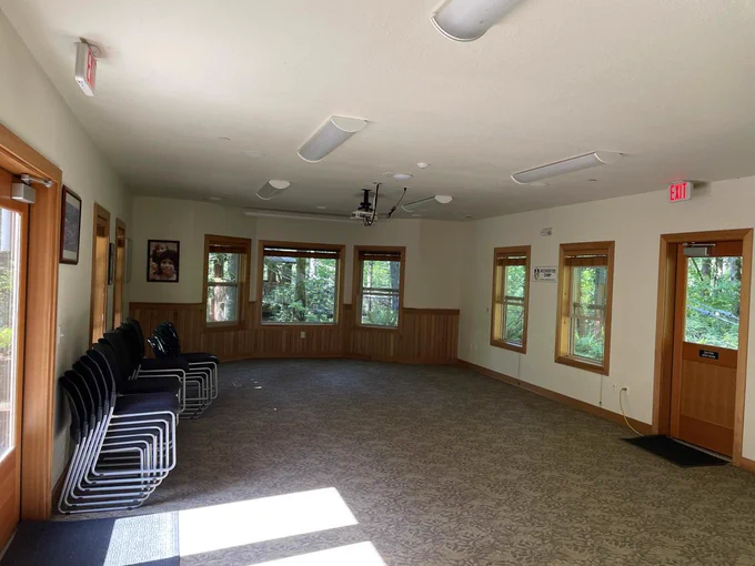 patterned gray brown carpeting, open floor space, wooden crown moulding and windowsills. a brown wooden archway and closet with closed doors in the back. black chairs are stacked to the left side of the photo.