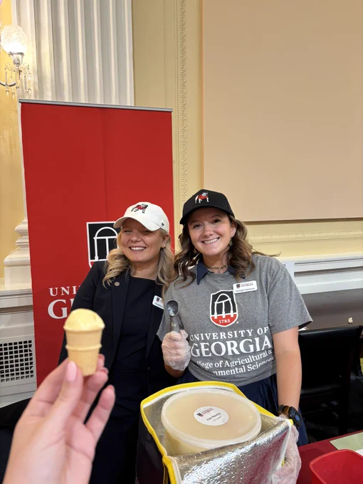 Two women pose as someone hands them an ice cream cone.