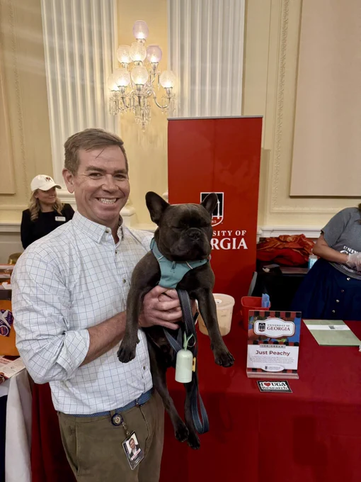 A man holding a small dog in front of UGA’s Scoops for Science table.