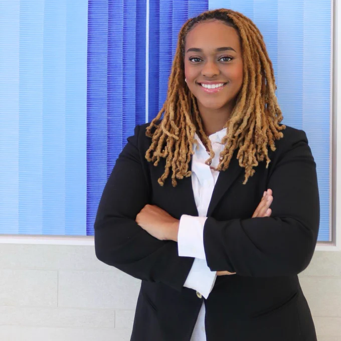 Chelsea Bolton standing in front of a blue painting with her arms folded.