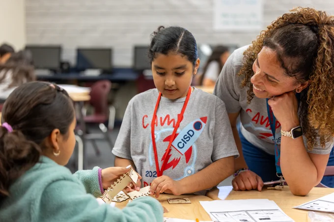 Two students and a teacher are in a classroom engaged in a collaborative STEM activity involving wooden pieces. 