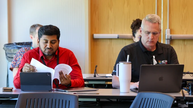 Two Center for Accelerated Application Readiness workshop participants review technical materials and work on laptops during a session focused on preparing scientific applications for the Discovery supercomputer.