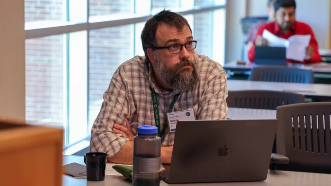 A workshop participant sits at a conference table with a laptop while listening to a presentation during the Center for Accelerated Application Readiness kickoff workshop.