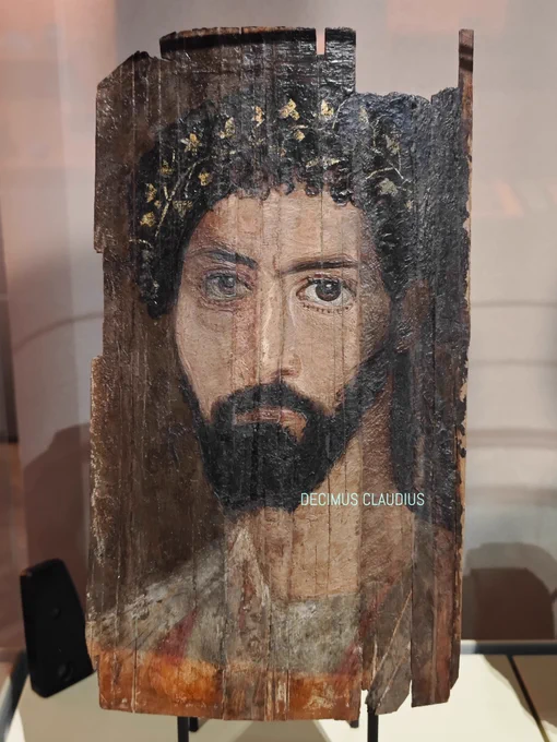 An Egyptian-Roman mummy portrait of a man dated to 150-200 AD.  "This serious looking man in a white tunic and cloak wears a wreath of vine leaves in his hair, a sign of divine status after death. His hairstyle is characteristic of the late 2nd century AD. Small curls hang decoratively over the forehead. This portrait appears to have undergone a number of (modern?) restorations. The two wooden fragments placed at an angle at the bottom on the right and the unusual colour contrasts in the face indicate this." Per a special exhibition's description. This is owned by the University of Heidelberg Egyptian Institute in Heidelberg, Germany which is closed for renovation.