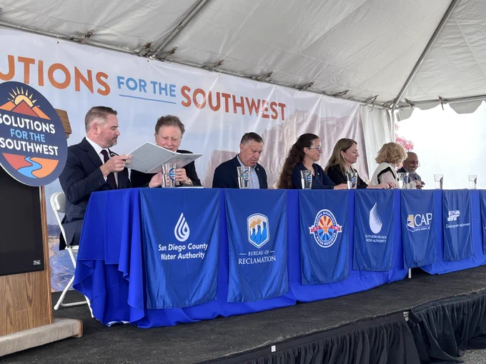 Representatives from Western water agencies participate in a memorandum of understanding signing ceremony beneath a “Solutions for the Southwest” backdrop. Agency banners line the table as officials review and sign documents supporting regional collaboration on water reliability and sustainability.
