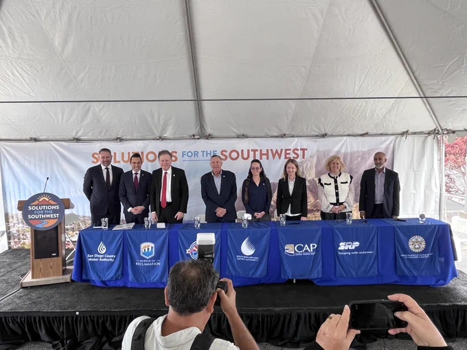 Representatives from the Bureau of Reclamation and partner water agencies pose for a group photo following a regional water partnership signing ceremony. The officials stand behind a table displaying agency banners beneath a “Solutions for the Southwest” backdrop, highlighting collaboration on long-term water reliability and sustainability across the Colorado River Basin.