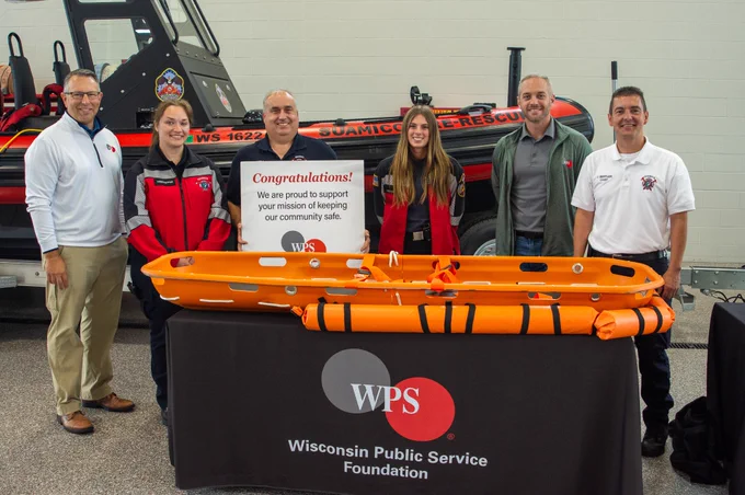 A group of men and women smile for a photo behind an orange water rescue basket lying on top of a table covered by a black WPS Foundation tablecloth.