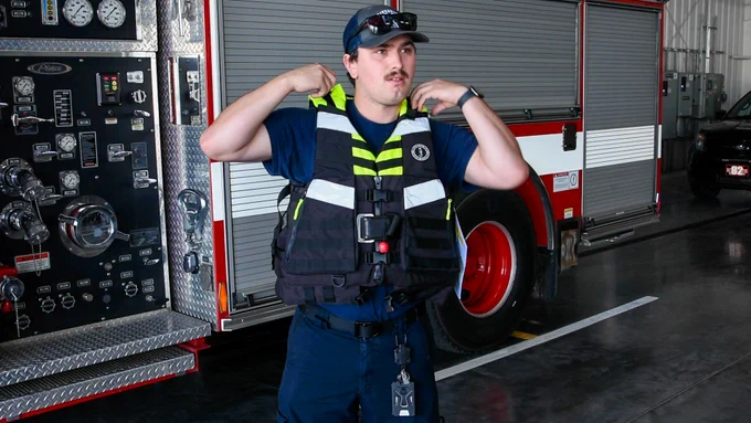 A firefighter tries on a yellow, black and white water rescue life jacket.