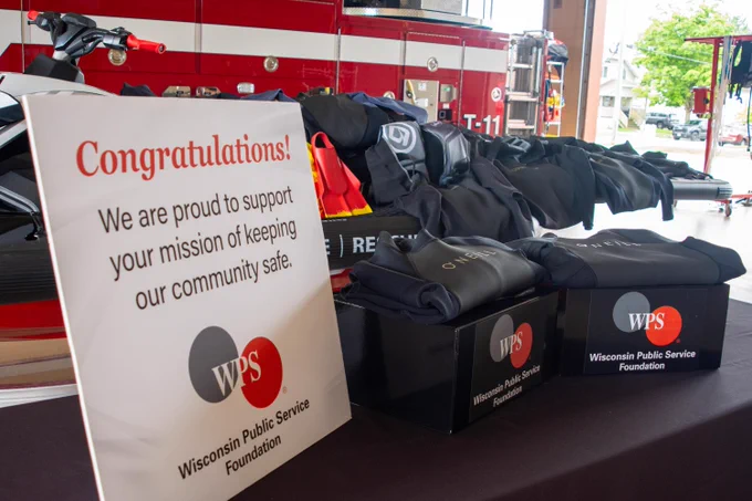 A congratulatory sign from the WPS Foundation is next to a row of water rescue wet suits in front of a fire engine.