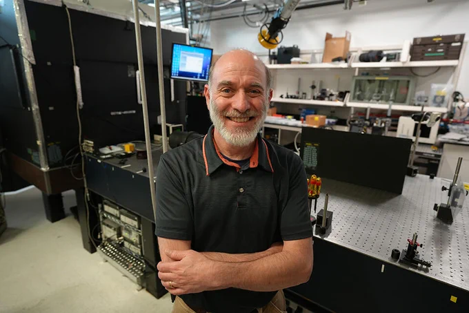 A man poses smiling in a laser laboratory.
