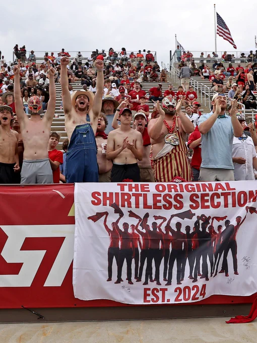 Enthusiastic fans in the shirtless section cheer at a sporting event. They display excitement and camaraderie.