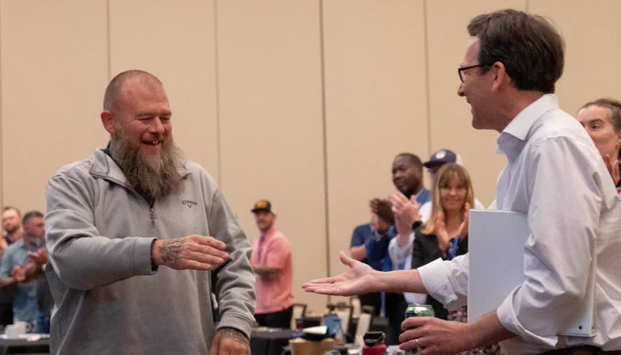 Bob reaching out to shake hand of individual while walking up to stage, others applauding in background