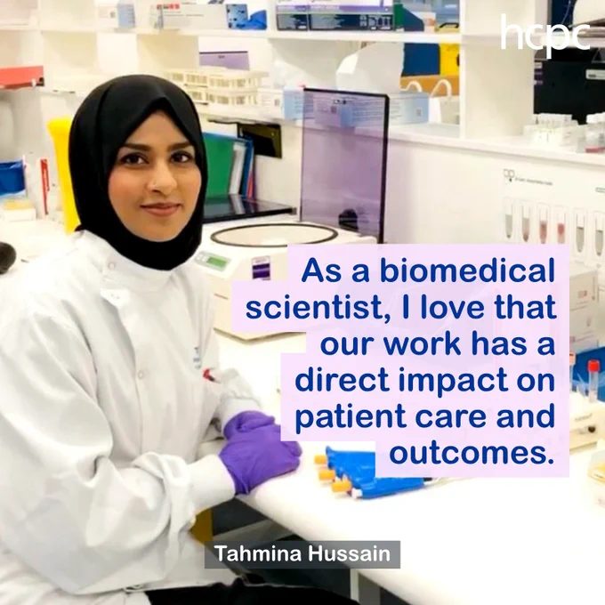 Biomedical scientist wearing lab coat and purple gloves working in a clinical laboratory surrounded by scientific equipment.