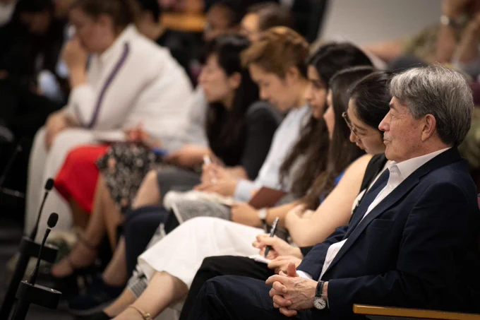 A group of people seated in a row attentively listening during a formal event or presentation.