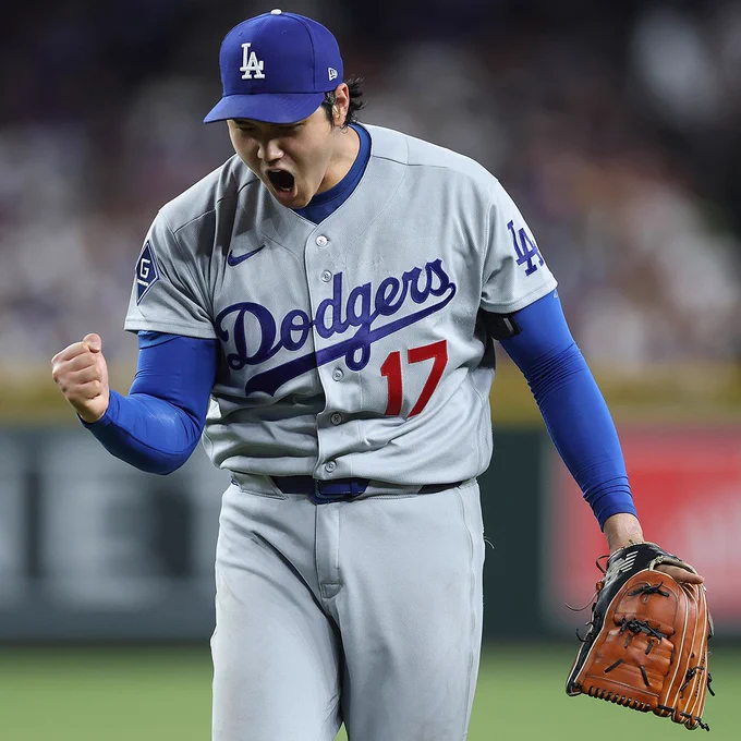 Shohei Ohtani shouts in celebration while walking off the mound. He is wearing a gray Los Angeles Dodgers jersey and a blue Dodgers cap.