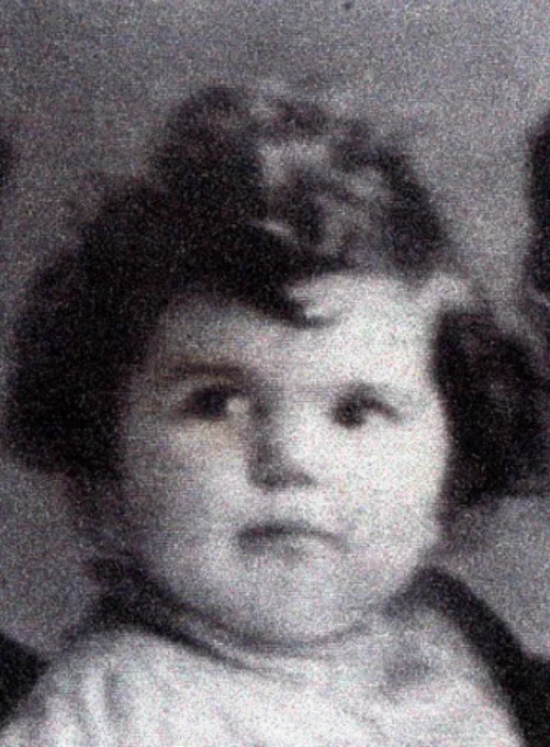 Black and white vintage photo of a young girl with curly hair looking directly at the camera.
