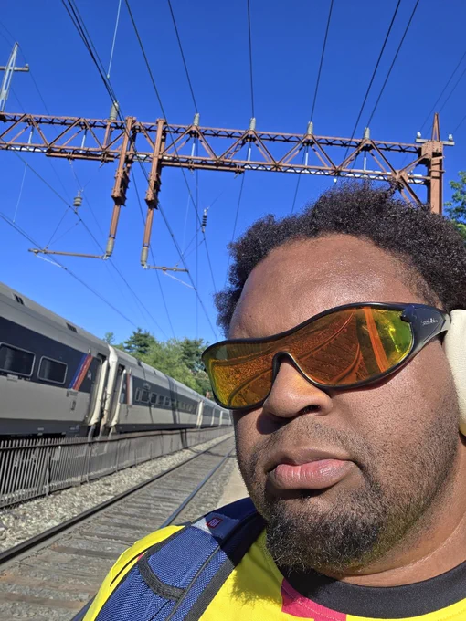 A selfie of me wearing sunglasses and headphones as an NJ Transit train passes by