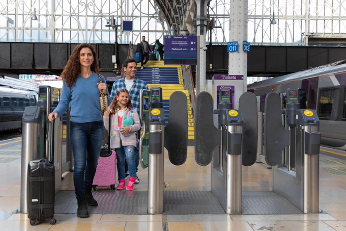 A family with a young child walking through the ticket gates on the platform at Paddington Station.