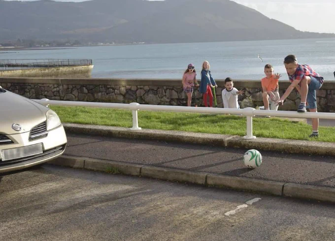 Image of children at the seaside playing with a ball beside a road. 