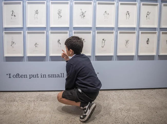 A young boy crouching to look at illustrations in the new Quentin Blake exhibition Performance at the brand new Quentin Blake Centre for Illustration, London. Photo by Justin Piperger