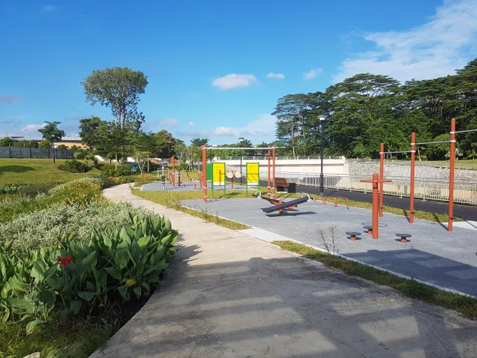 Outdoor fitness park with exercise equipment under a clear blue sky surrounded by greenery and trees.