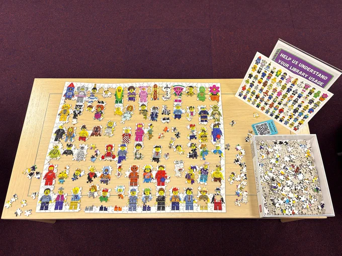 A partially completed lego minifigures jigsaw set out on a table.
