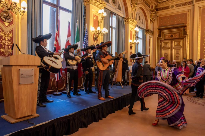 A mariachi band plays on stage with two dancers in front of them.
