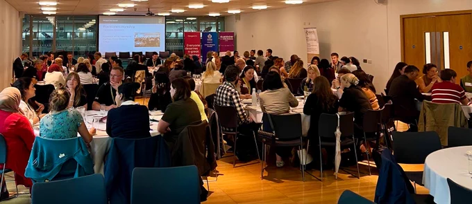 Large group of people seated at round tables in a conference room, engaged in discussions during a workshop or seminar.