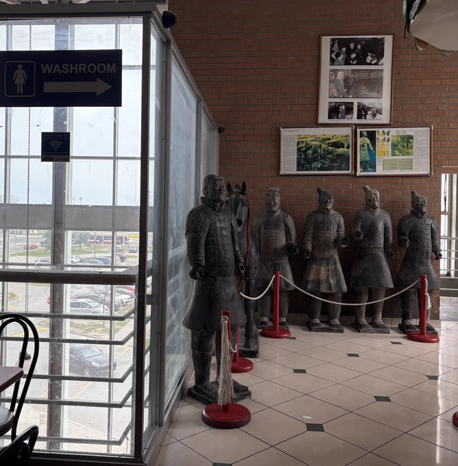 Terracotta warrior replica statues standing beside a washroom sign.