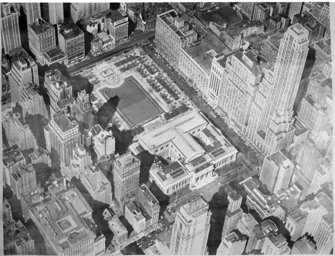 Aerial view of a dense urban area with tall skyscrapers and Bryant Park surrounded by buildings.