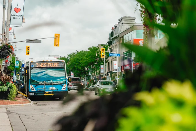 City bus labeled '3 Westmount' driving through a busy urban street with traffic lights and cars under a cloudy sky.
