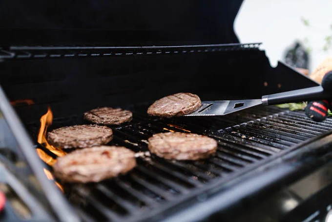 Close-up of beef patties grilling on an outdoor barbecue. Perfect for summer cookouts.