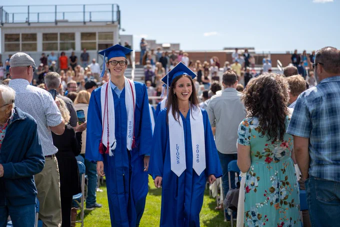 Lyons Middle Senior High School seniors wearing blue robes and graduation caps approach the stage.
