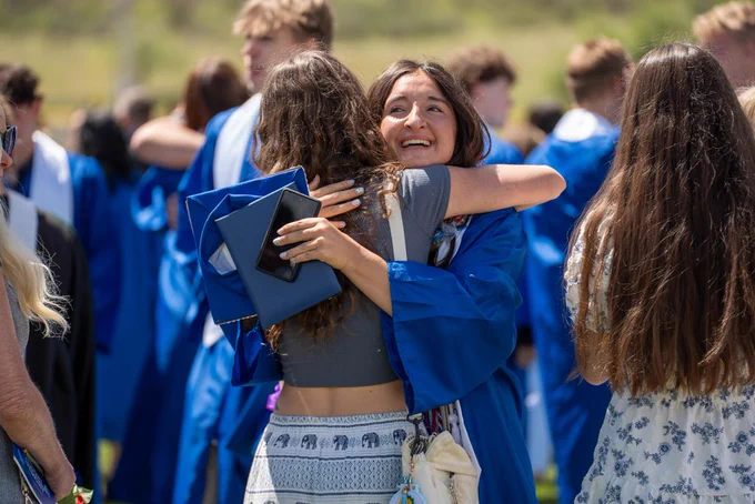 A Lyons Middle Senior High School senior wearing blue robes hugs a family member.
