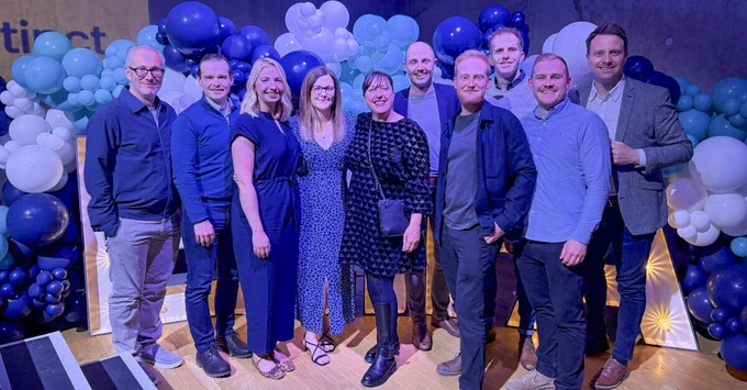 Group of attendees posing together in front of a blue and white balloon backdrop at an event.
