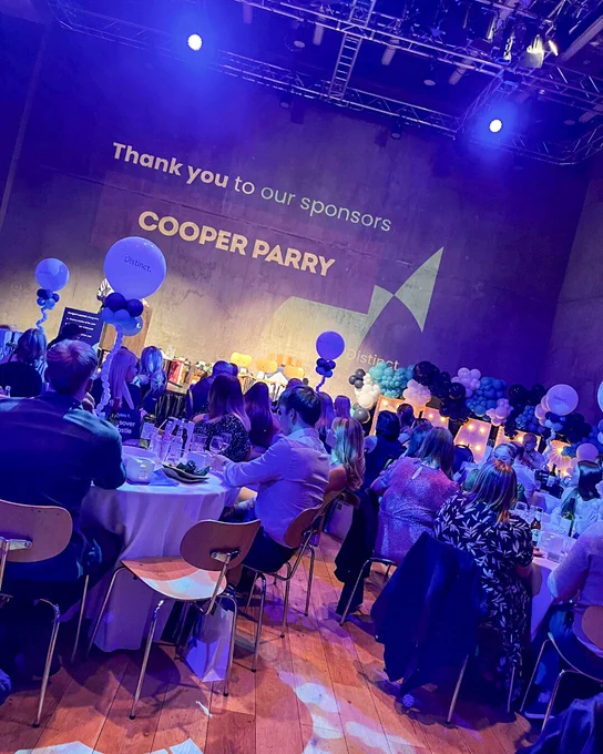 Event stage with “Thank you to our sponsors – Cooper Parry” displayed, audience in foreground under blue lighting.
